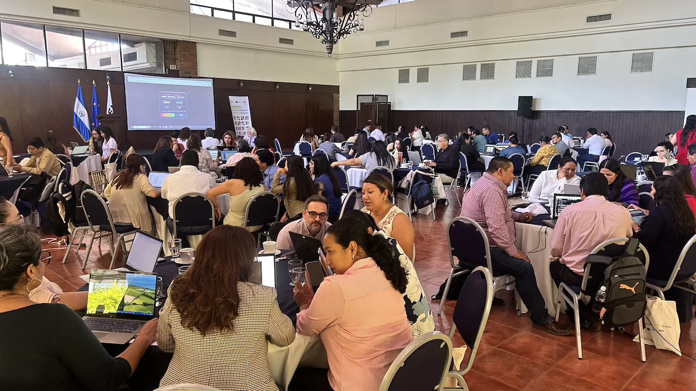 A room full of advisors working in teams on their computers during the program's closing day in San Salvador
